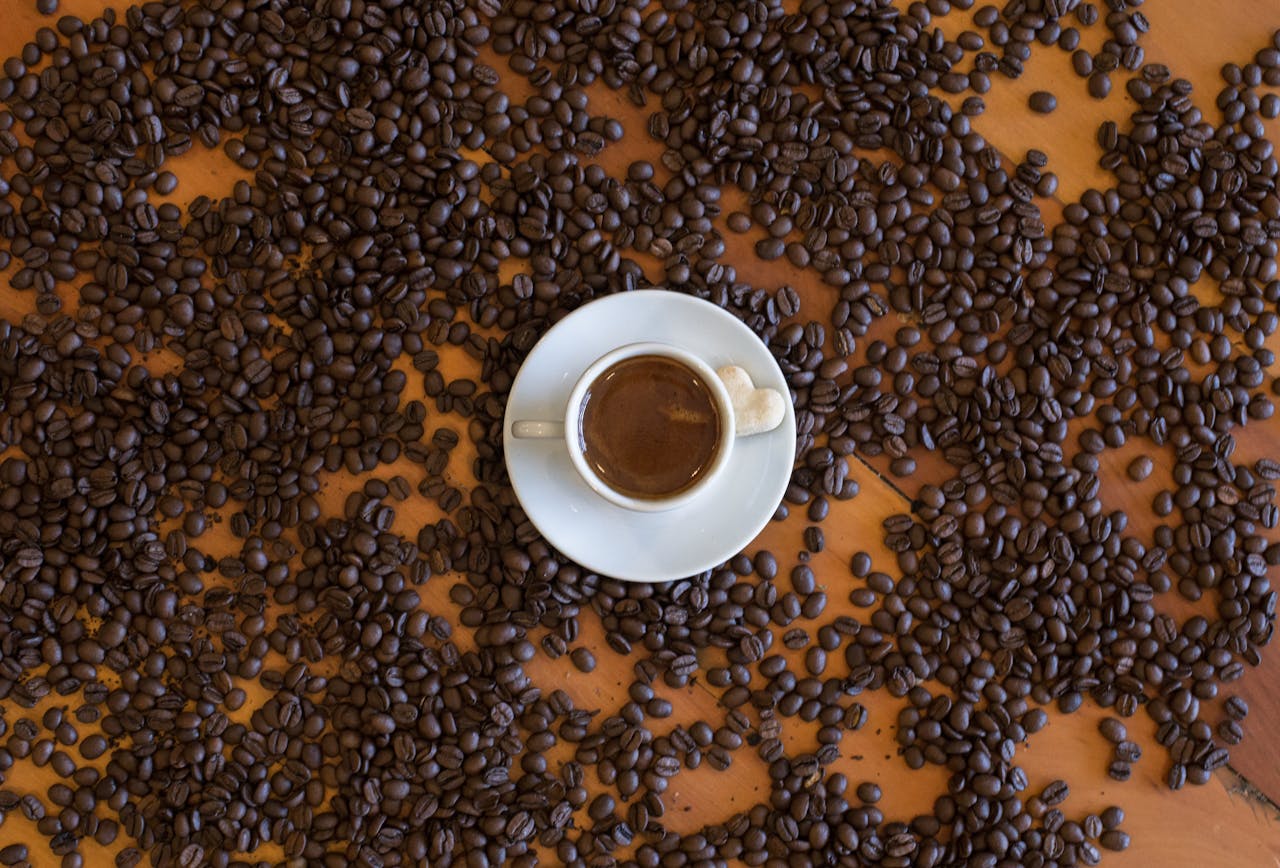 TUTORIAL CHAPTER 2 A top view of an espresso cup on a wooden table, surrounded by scattered coffee beans.