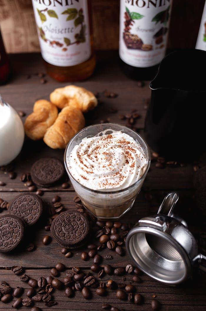 From above composition of delicious coffee with whipped cream served on wooden table near coffee beans and chocolate cookies in cafeteria