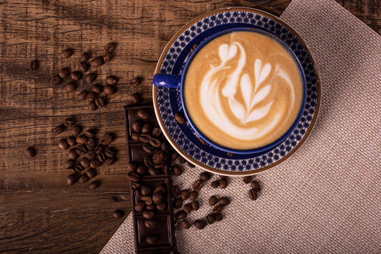 A beautifully crafted latte with latte art, surrounded by coffee beans and chocolate, shot from above.